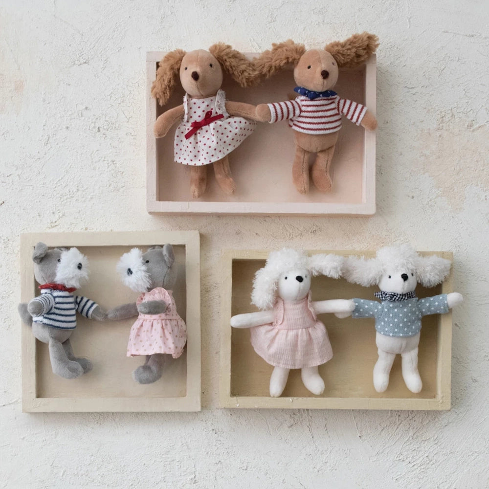 Three pairs of dressed stuffed dog dolls in small wooden shadow boxes mounted on a textured white wall.