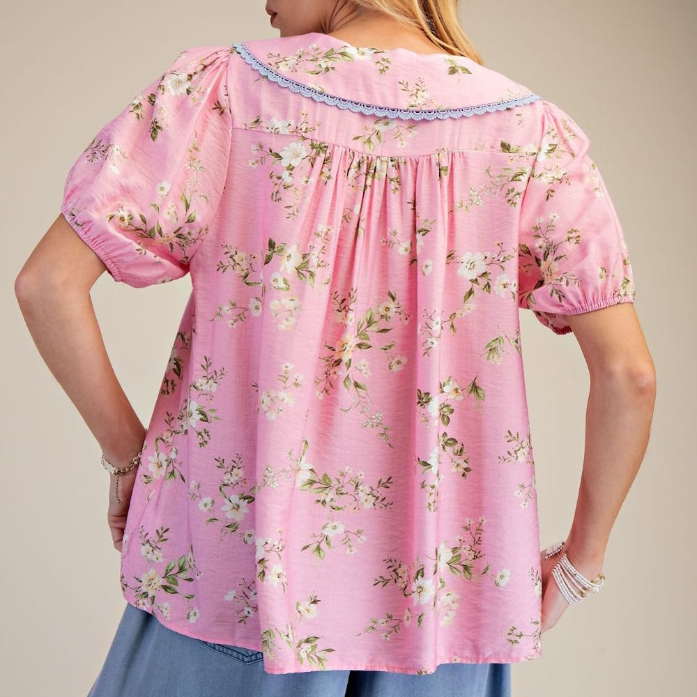 Back view of a women's pink floral cotton top with short puff sleeves, a ruffled collar, and pleated back detailing.