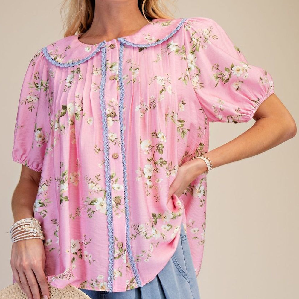 Pink short-sleeve floral cotton blouse with a Peter Pan collar, blue lace trim, button-front, and puffed sleeves.