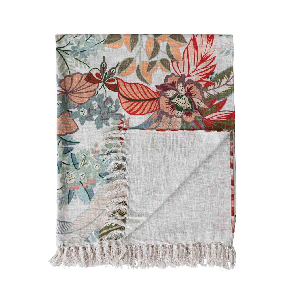 Cotton printed throw blanket with tropical botanical patterns, vibrant flowers, and fringe edge on a white background.