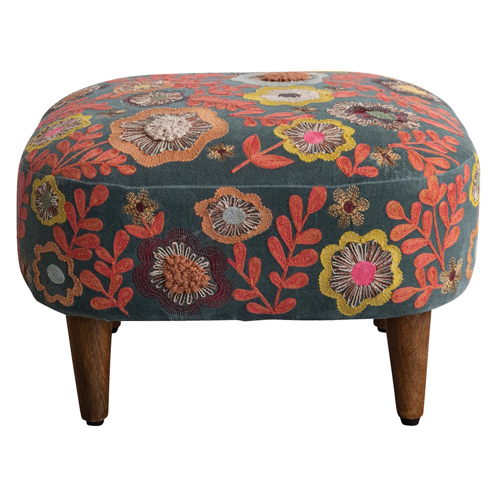 A low velvet stool with colorful embroidered flowers and short wooden legs on white background.