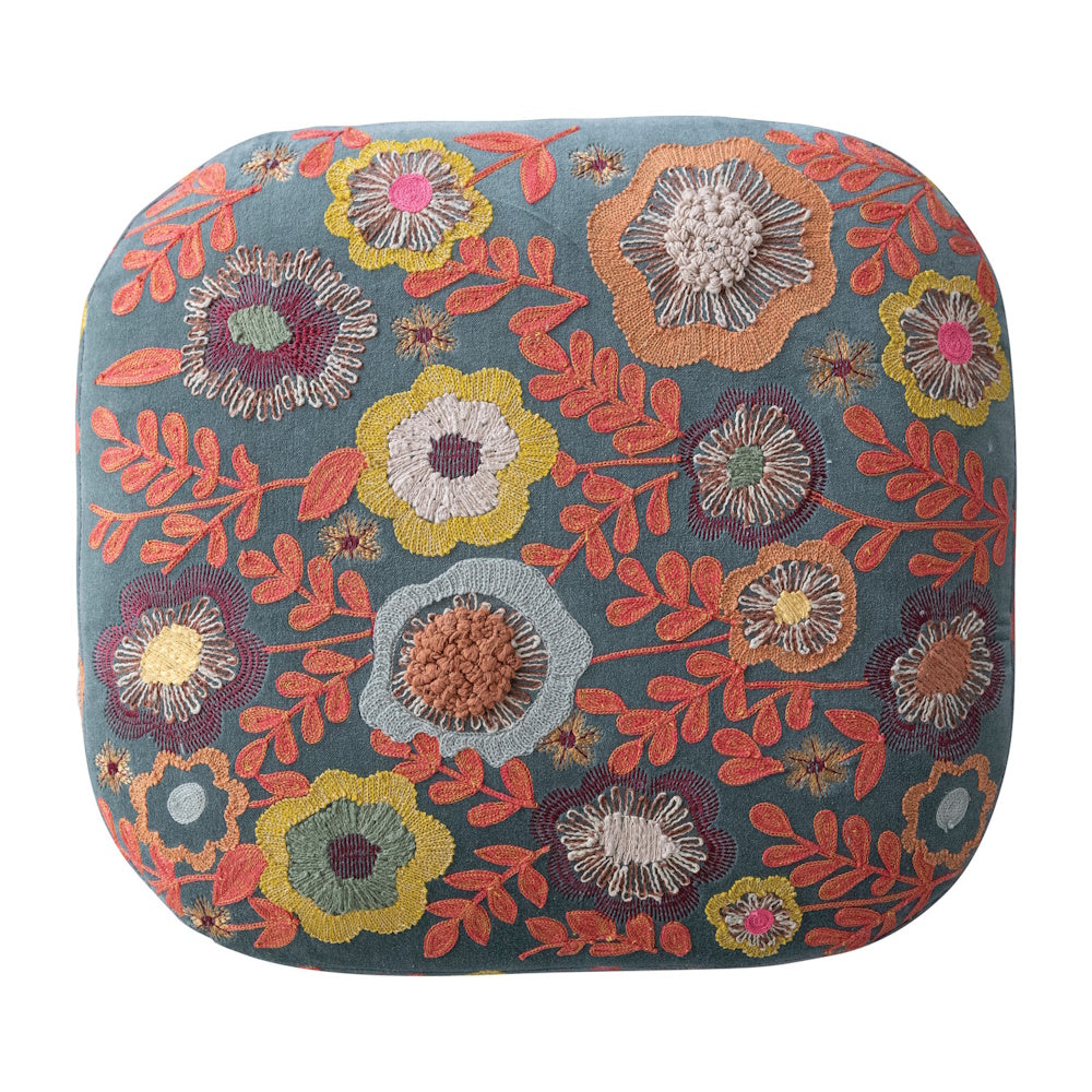 A top-down view of a blue velvet stool cushion embroidered with colorful textured flowers and orange vines.