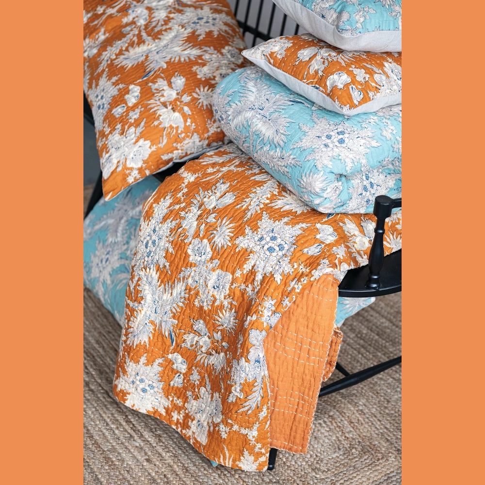 Floral cotton voile bed cover and king shams in orange and blue with white botanical prints on a black chair.