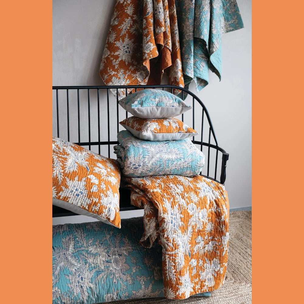 Floral cotton voile bed cover and king shams with blue and mustard yellow botanical patterns on a black metal bench.