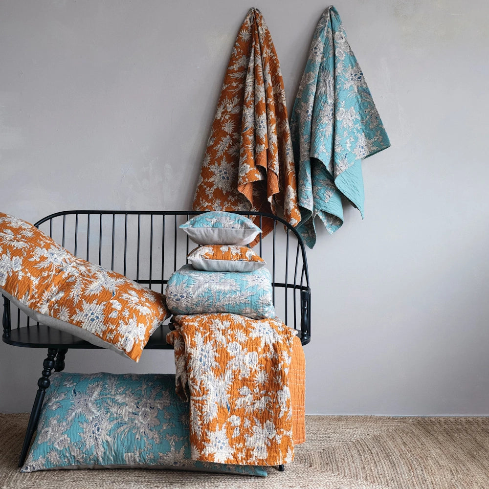 Floral cotton voile bed cover and shams in orange and teal draped over a black bench with floral patterns.