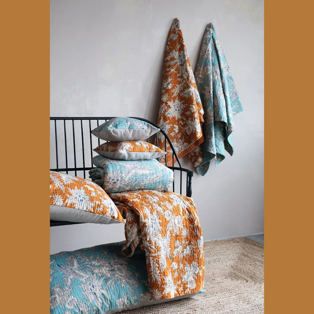 Floral cotton voile bed cover and king shams with blue and mustard yellow botanical patterns on a black metal bench.