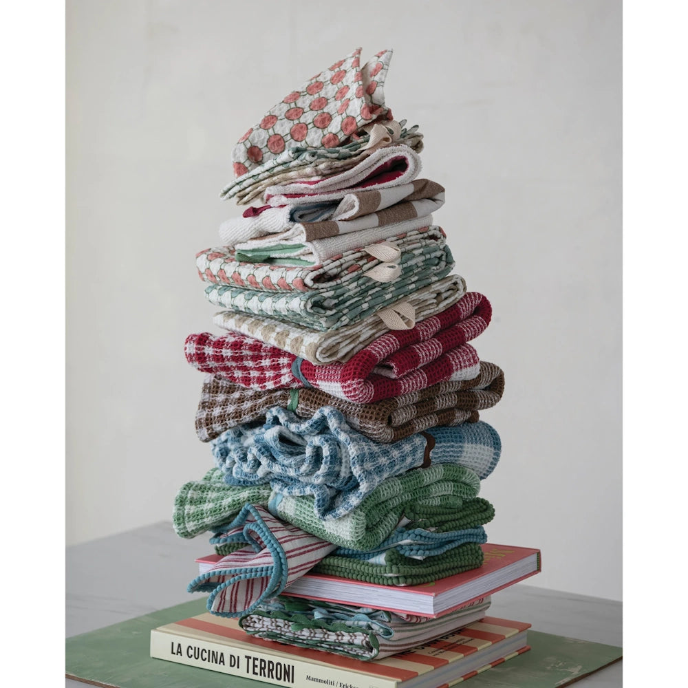 Tall stack of folded and patterned waffle-weave tea towels balanced on a pile of cookbooks.
