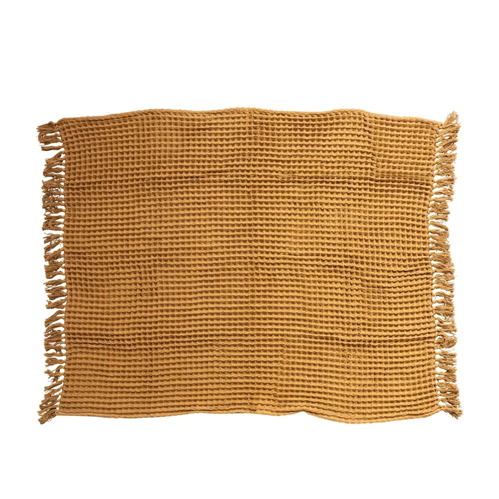 Folded textured cotton waffle weave throw blanket with fringed edges on a plain white background.