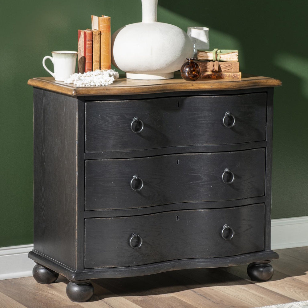 Black three drawer accent chest with curved fronts, ring pulls, bun feet, and styled tabletop decor.