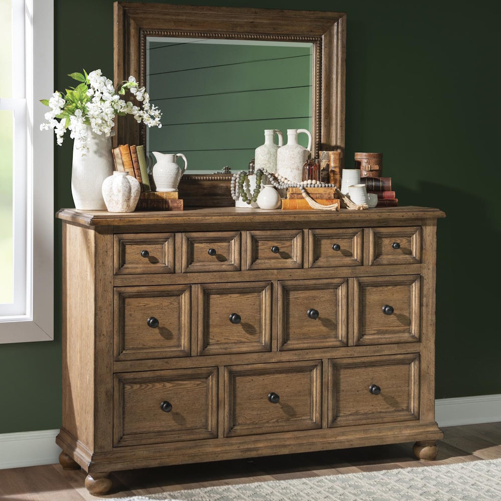 Rustic wood dresser with eight paneled drawers, styled with books, pottery, flowers, and a framed mirror.