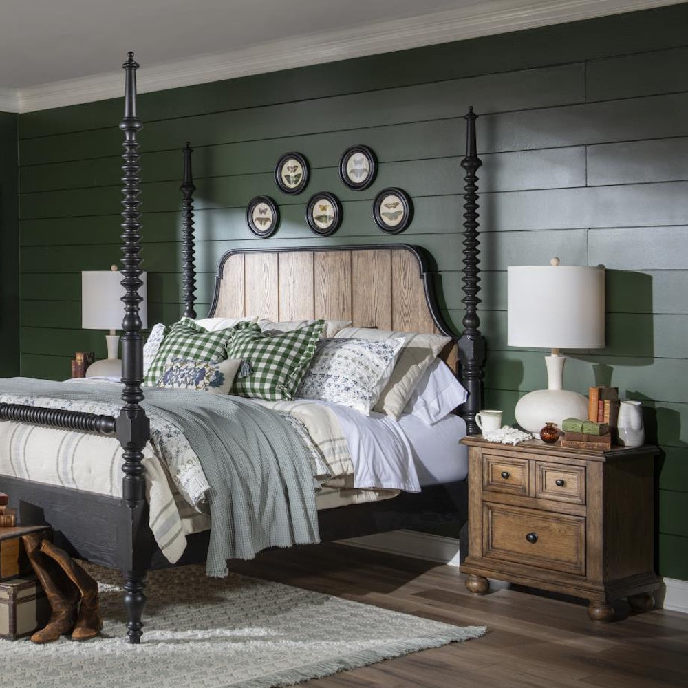 Rustic bedroom with black poster bed, wooden nightstand, white lamps, and dark green paneled wall.