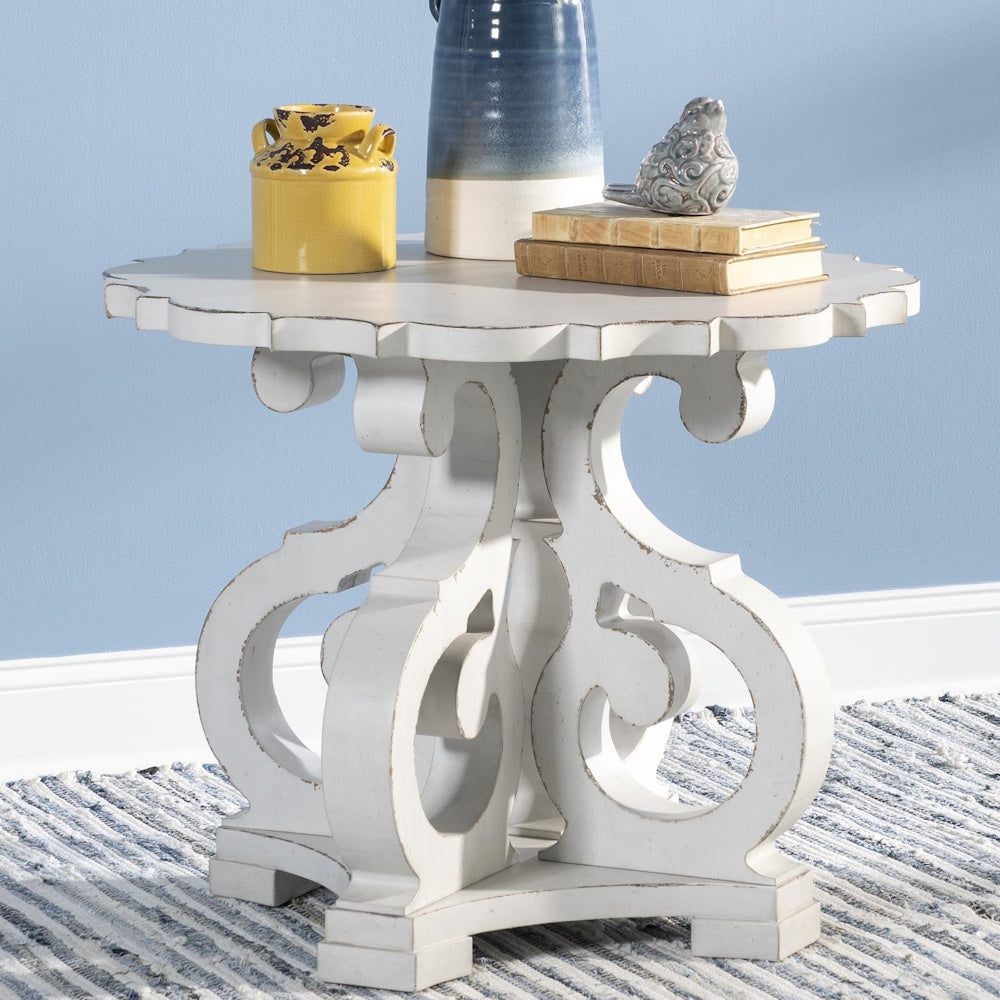 White distressed end table with ornate scrollwork base, styled with ceramic vases and stacked books.