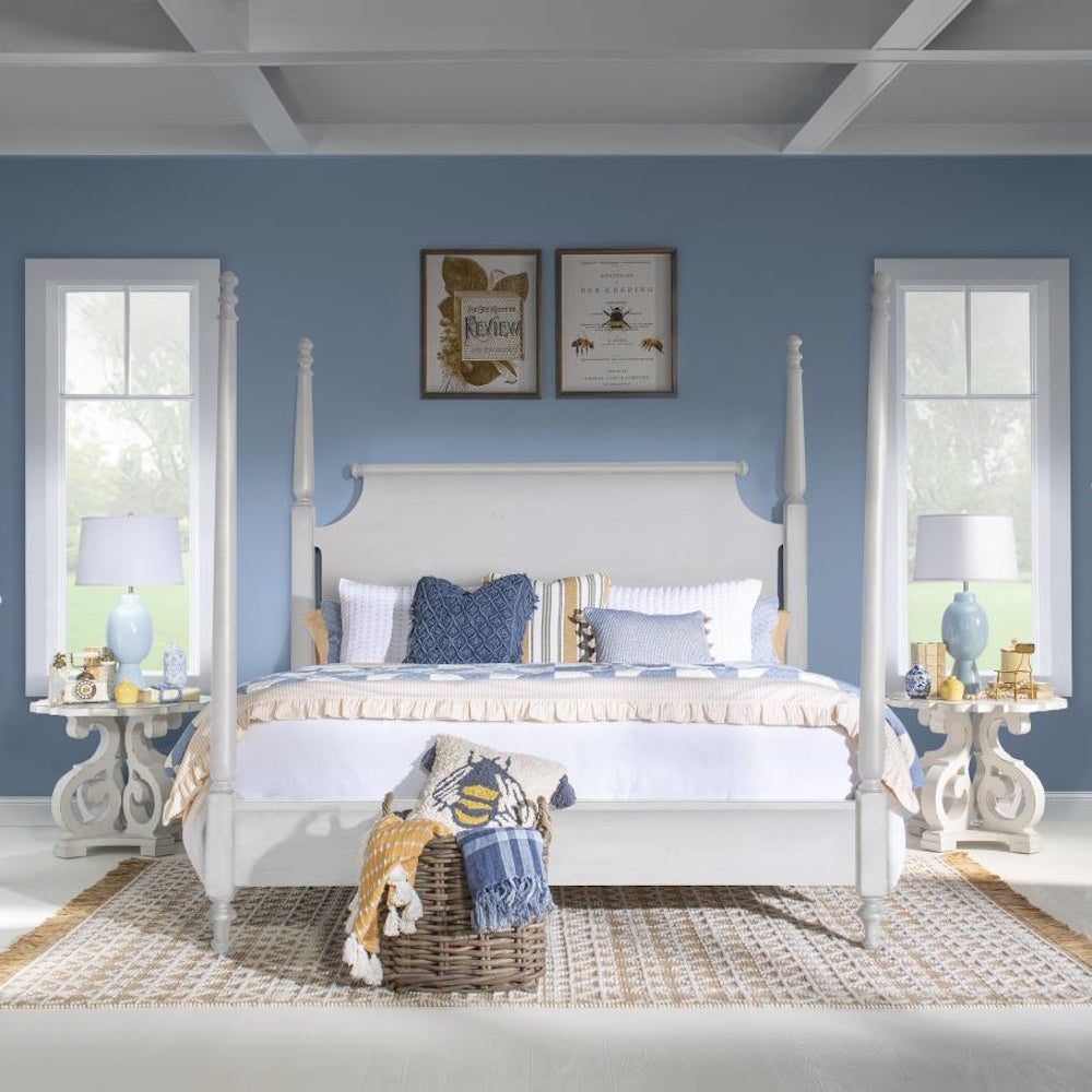 Bedroom with white four poster bed flanked by matching white scrollwork end tables and blue accents.