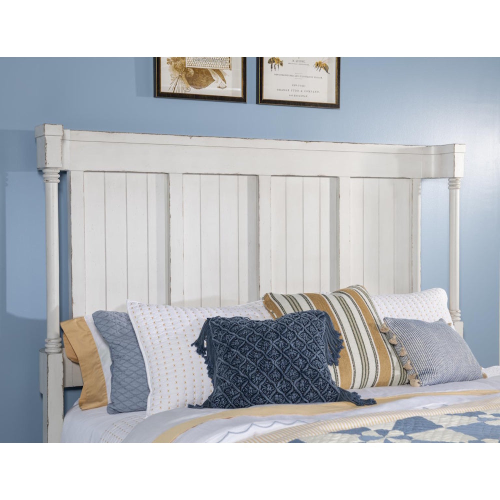 Close up of white paneled headboard with turned posts, styled with blue and striped accent pillows.