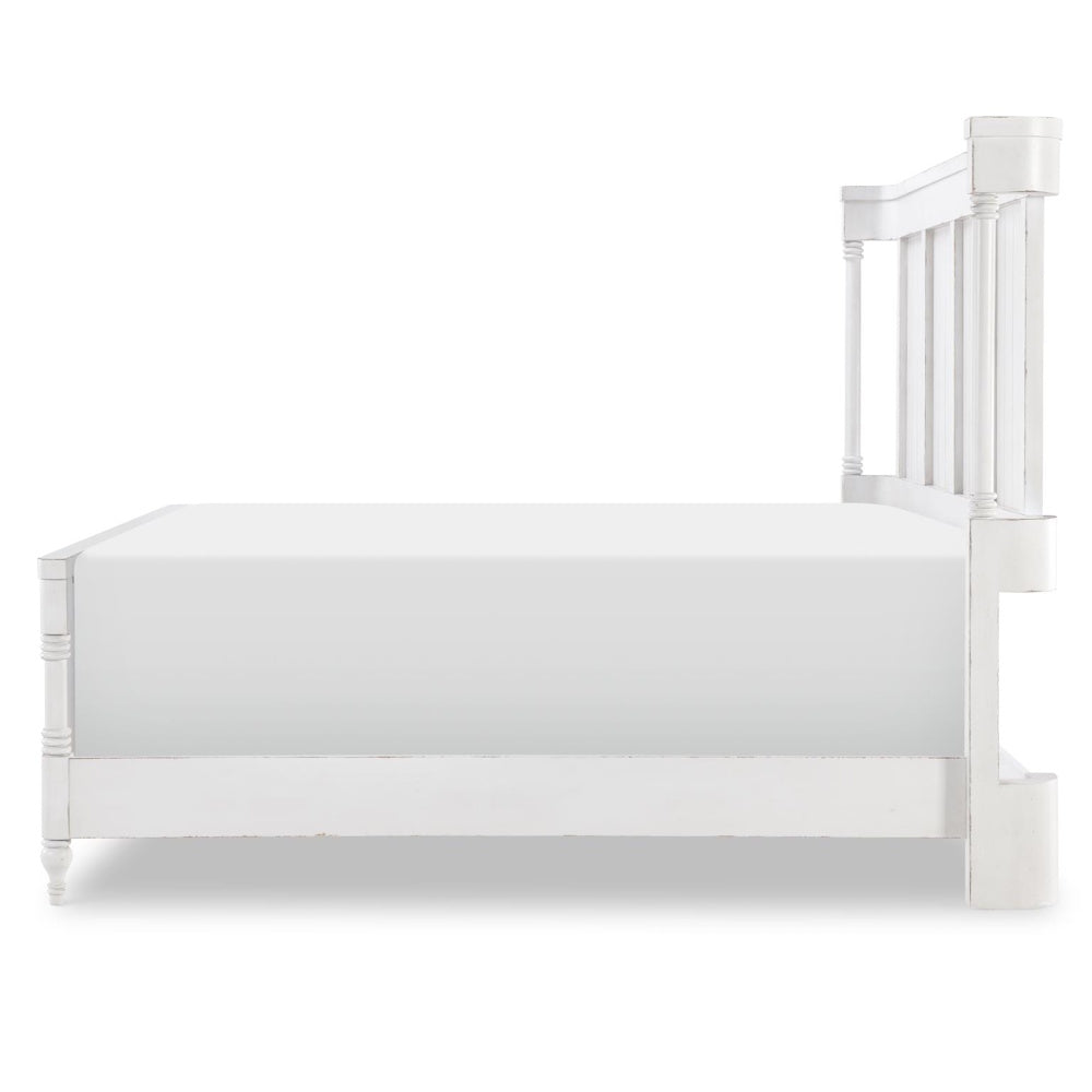 Side view of white queen bed with paneled headboard, turned posts, and distressed farmhouse finish.
