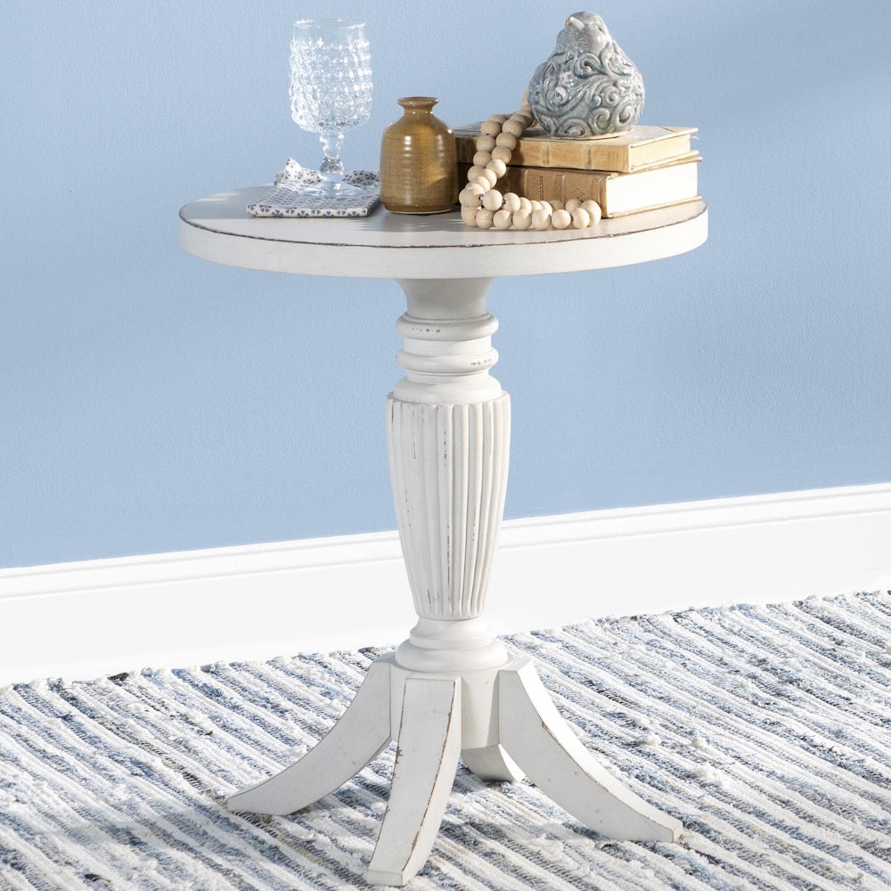 Round, distressed white wooden end table decorated with books and decor against a light blue wall.