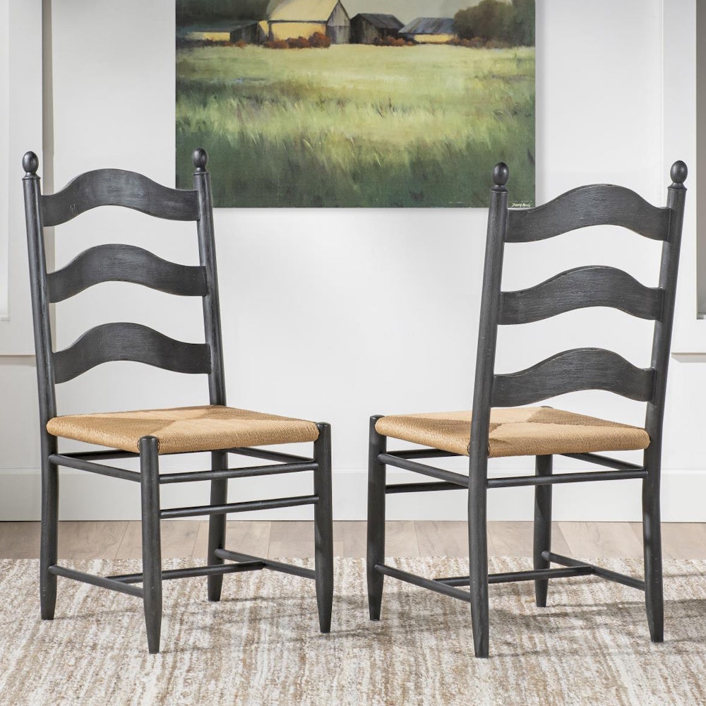 Two gray ladder-back chairs with woven rush seats displayed on a rug beneath a landscape wall painting.