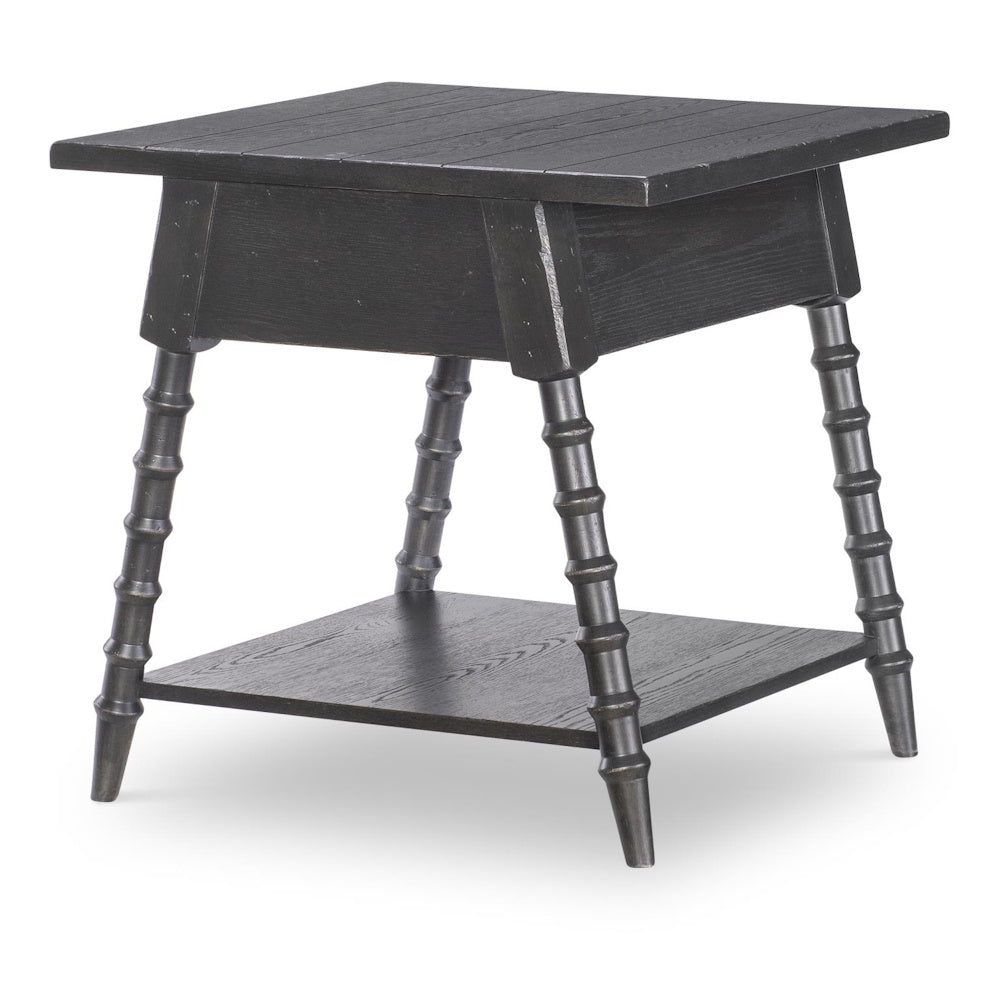 Black wood end table with splayed bobbin style legs, lower shelf, and plank top, shown from rear angle.