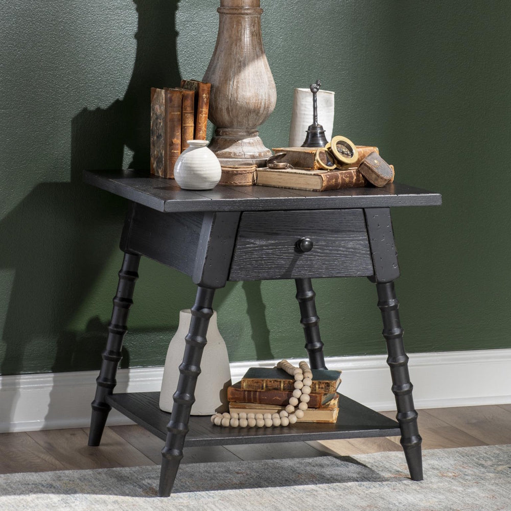 Black wood end table with bobbin style legs, drawer, and lower shelf, styled with books and decor.