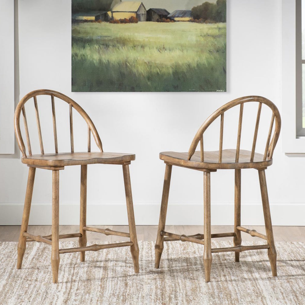 Two wooden Windsor counter stools facing each other on a textured rug beneath a landscape painting.