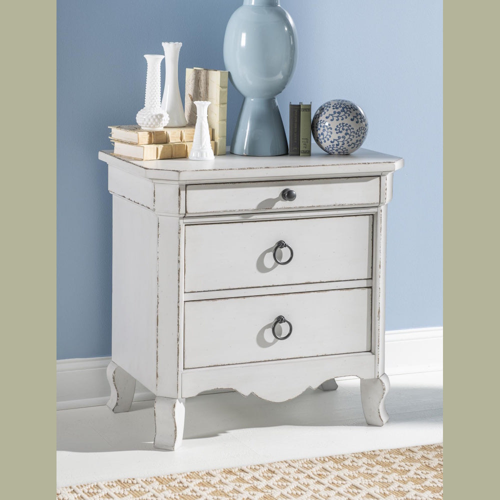White distressed 3-drawer nightstand with vintage decor on top against a blue wall.