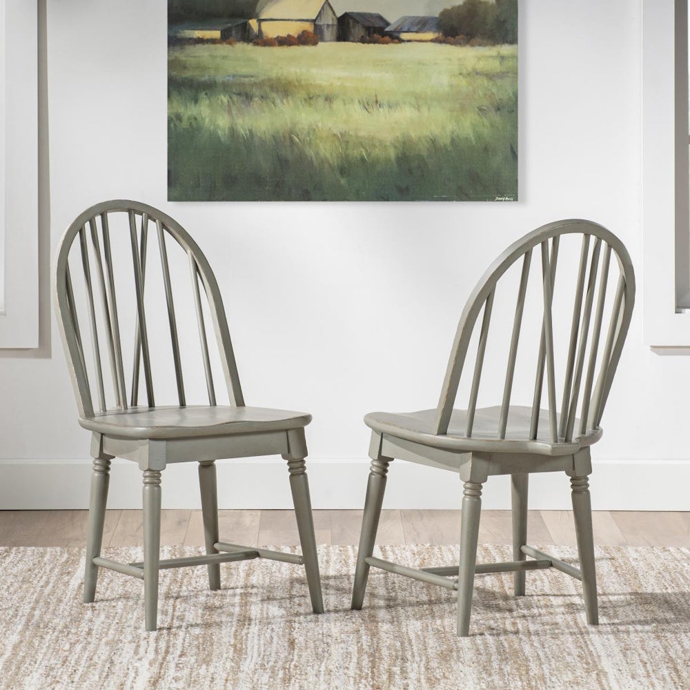 Two light gray Windsor side chairs with curved spindle backs on a textured rug beneath wall art.