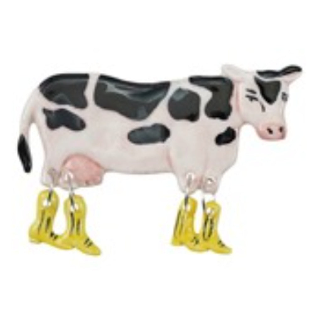 A black and white cow fridge magnet with four dangling yellow boots for legs on a plain white background.