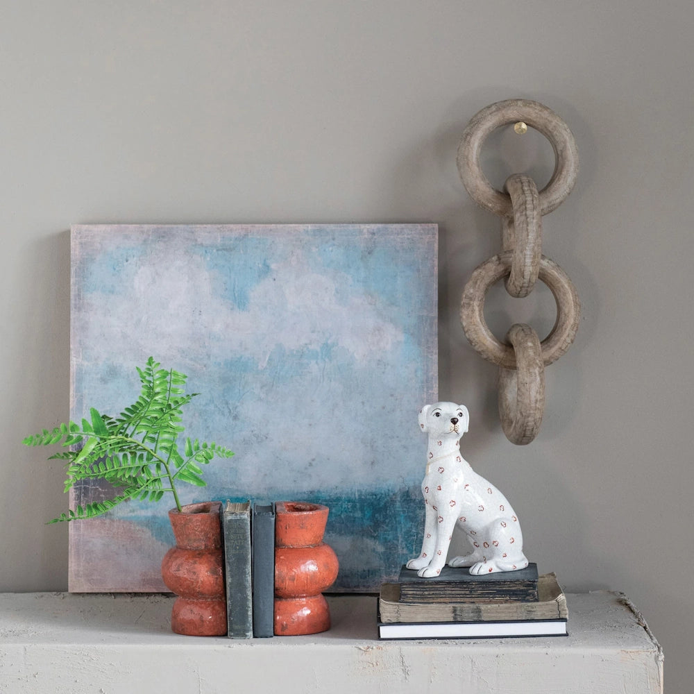 Hand-painted ceramic dog figurine with crackle finish on a stack of books, featuring rustic home decor and blue wall art.
