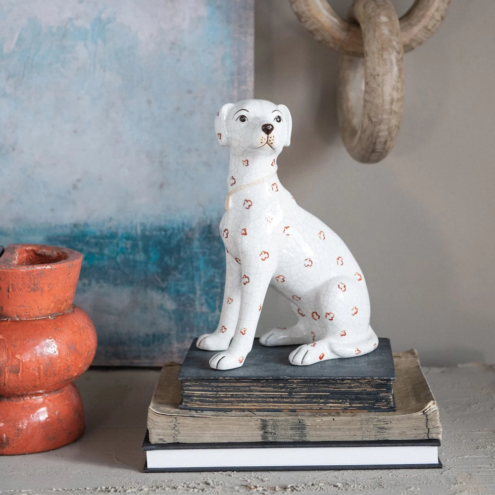 Hand-painted white ceramic dog figurine with a crackle finish and red floral patterns, sitting on a stack of vintage books.