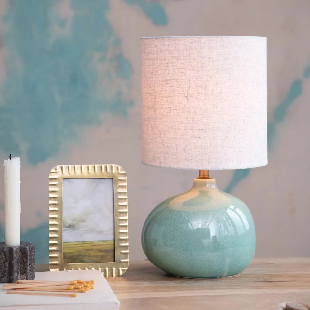 An organic-shaped, seafoam green crackle-glaze stoneware table lamp with a linen shade on a wooden table.