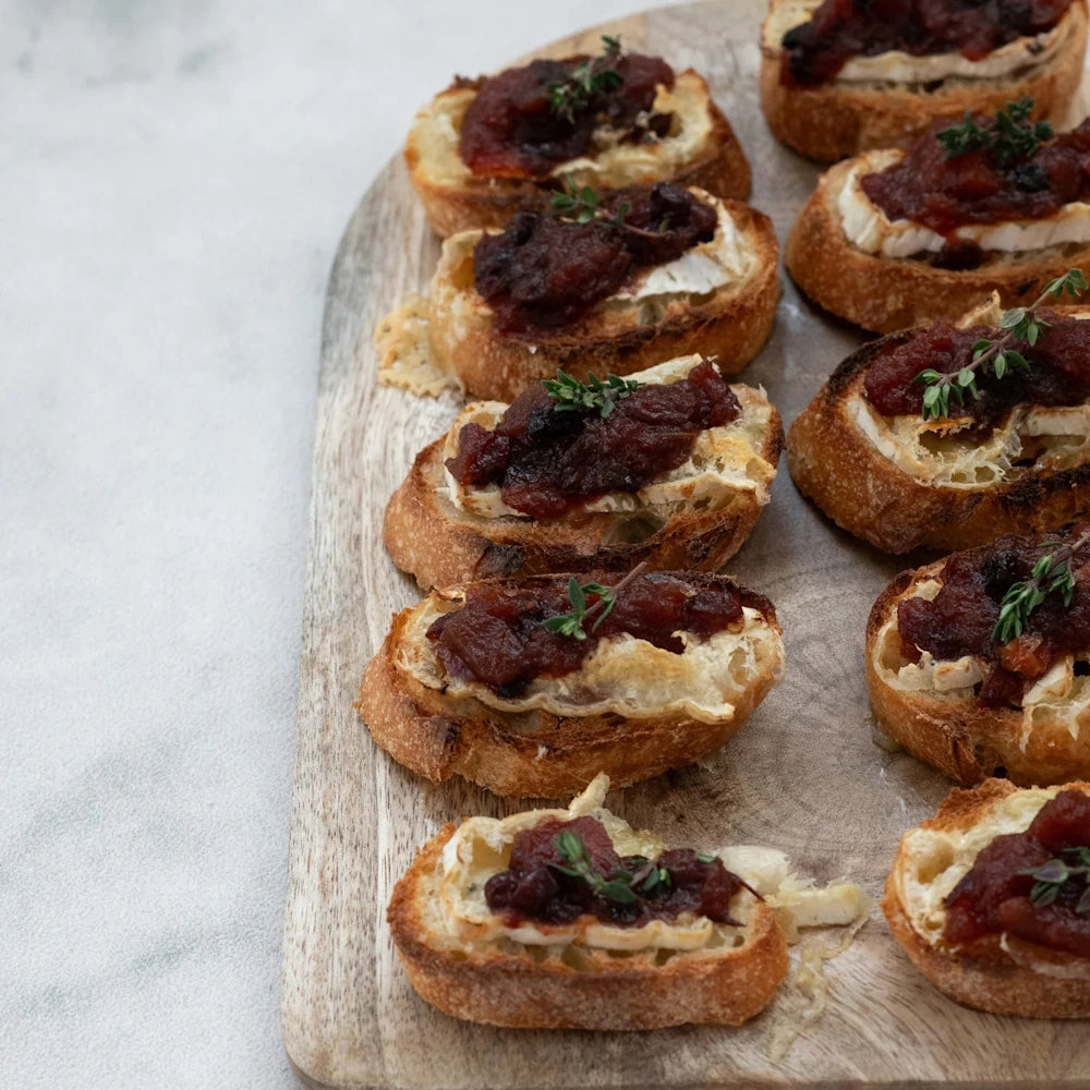 Toasted baguette slices topped with brie cheese and cranberry chutney on a wooden board.