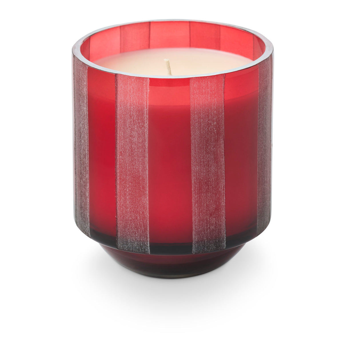 An unlit candle in a translucent red etched-stripe glass jar.