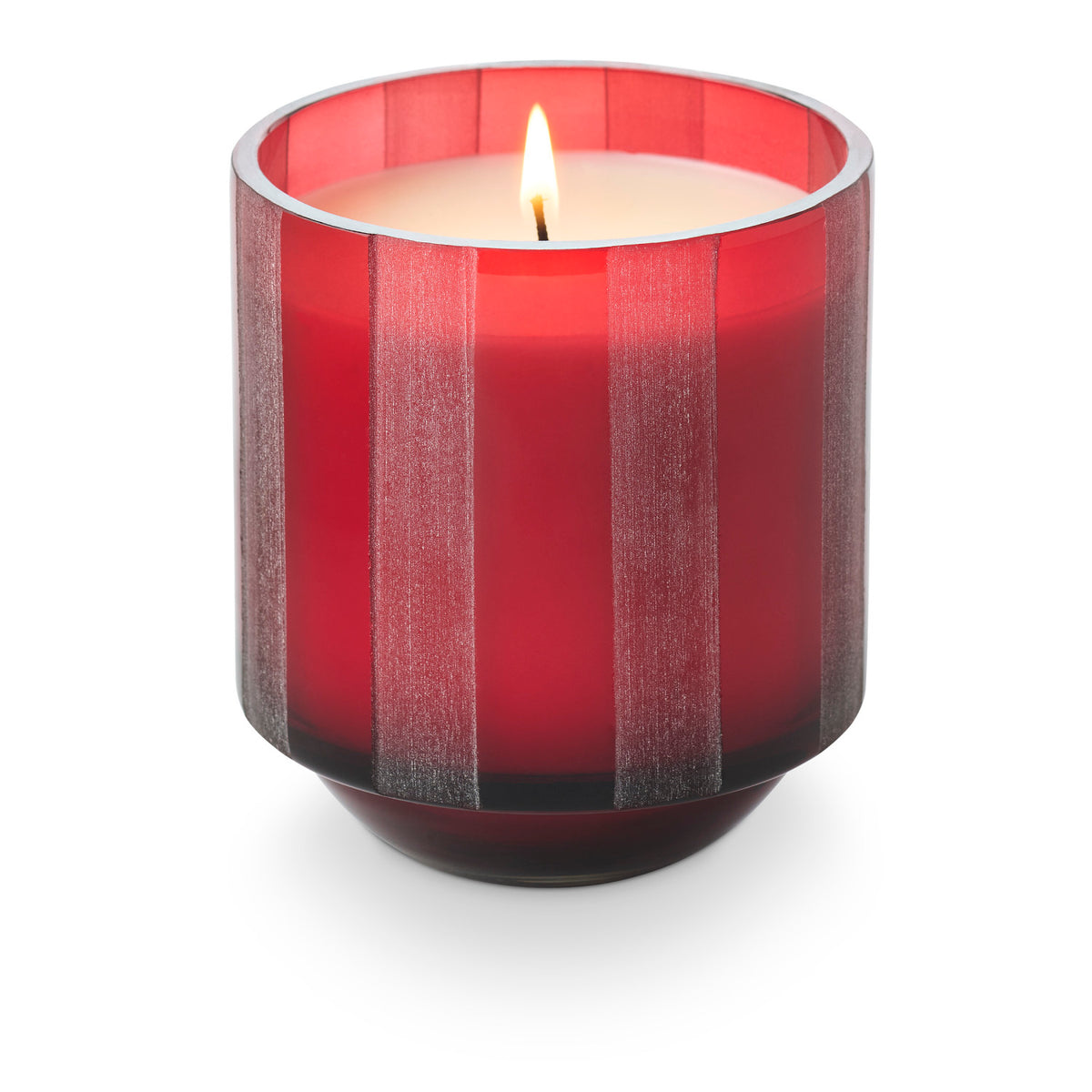A lit candle in a translucent red etched-stripe glass jar.