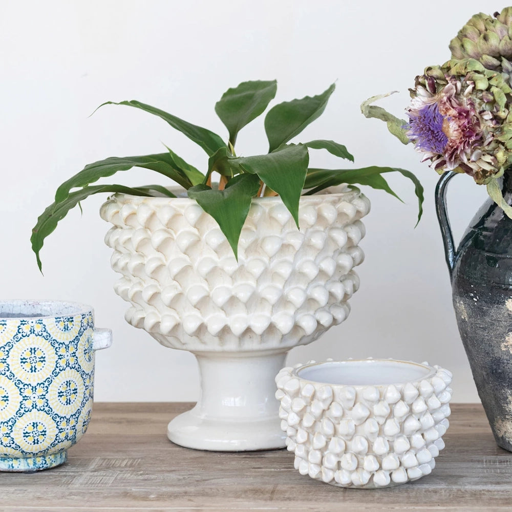 Handmade textured ceramic planters, white hobnail pedestal bowl, and decorative indoor plant pots on wood surface.