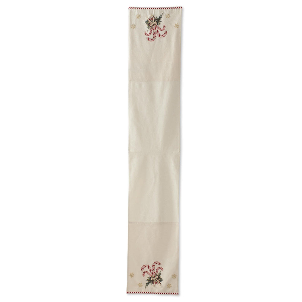 Cream holiday table runner with red and white candy canes, pine sprigs, a red ribbon, and gold snowflakes.