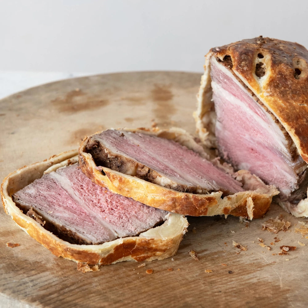 Sliced Beef Wellington with golden pastry crust and tender pink roast beef arranged on a wooden board.