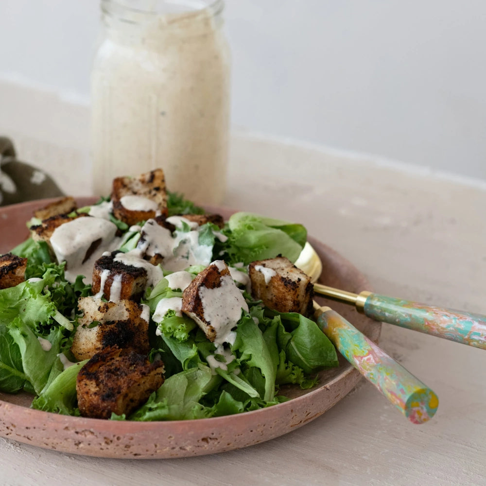 Fresh green salad topped with croutons and creamy dressing in a pink ceramic bowl, with a jar in the background.