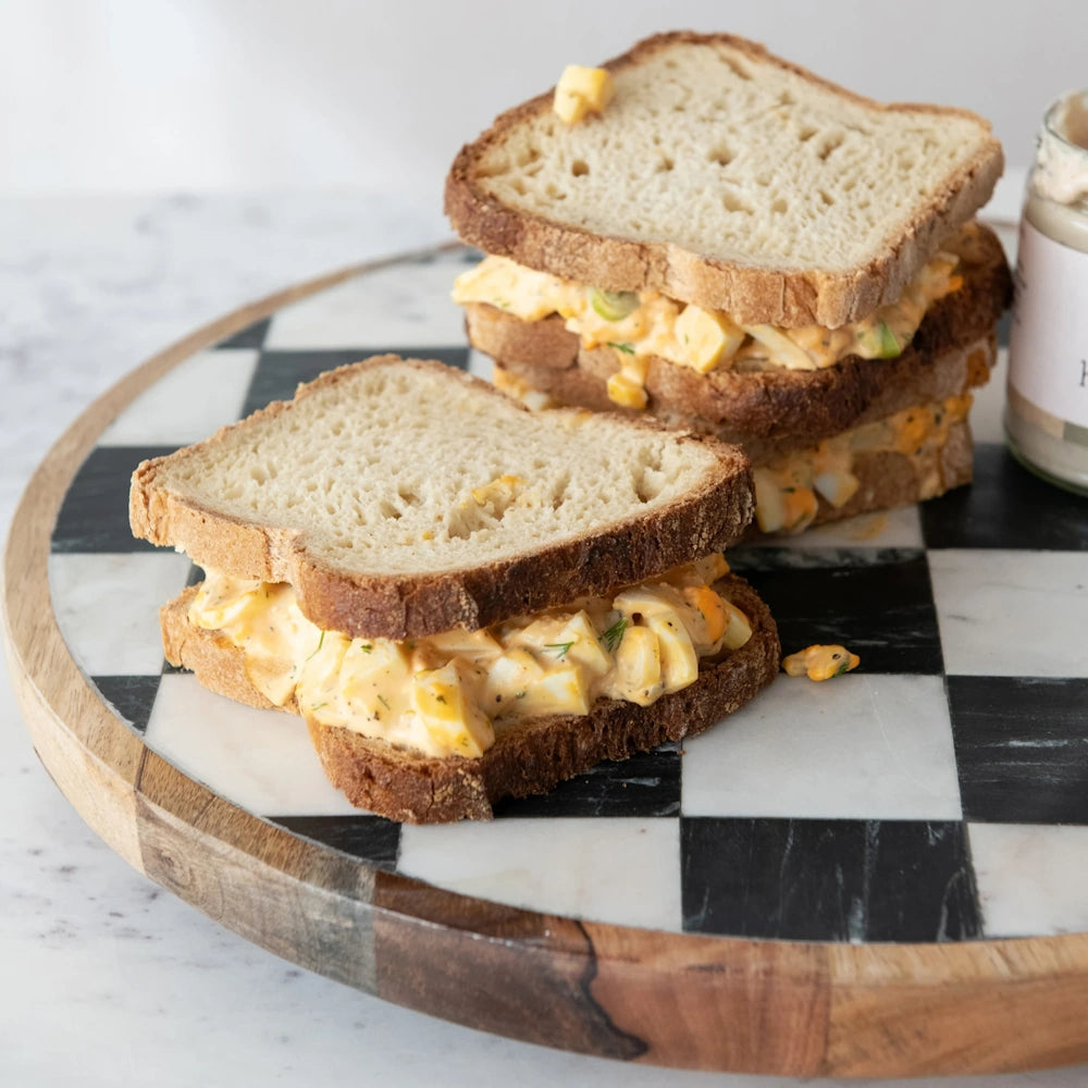 Egg salad sandwiches served on a black-and-white checkered round marble cutting board.