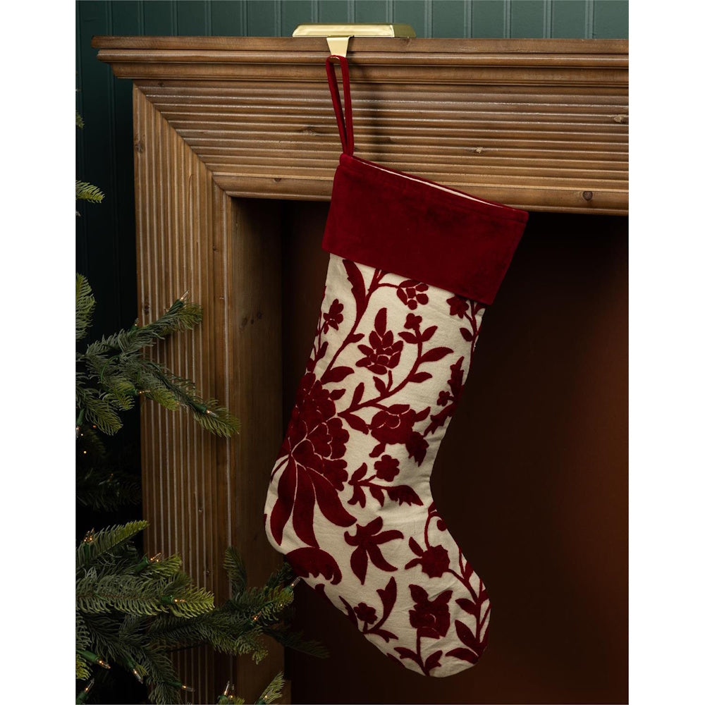 Cream Christmas stocking with red floral embroidery and velvet cuff hanging from a wooden mantel.