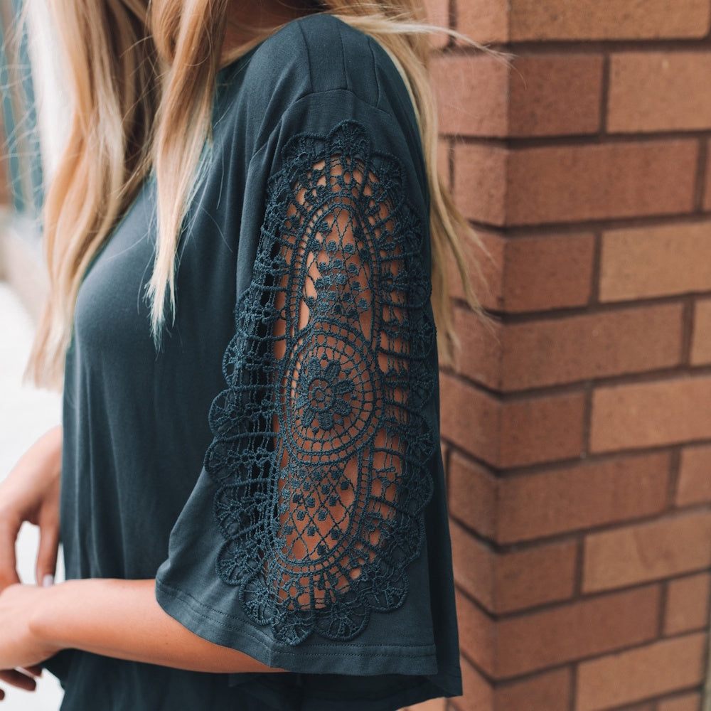 Close-up of a woman wearing a dark gray top featuring intricate lace crochet detailing on the short sleeve.