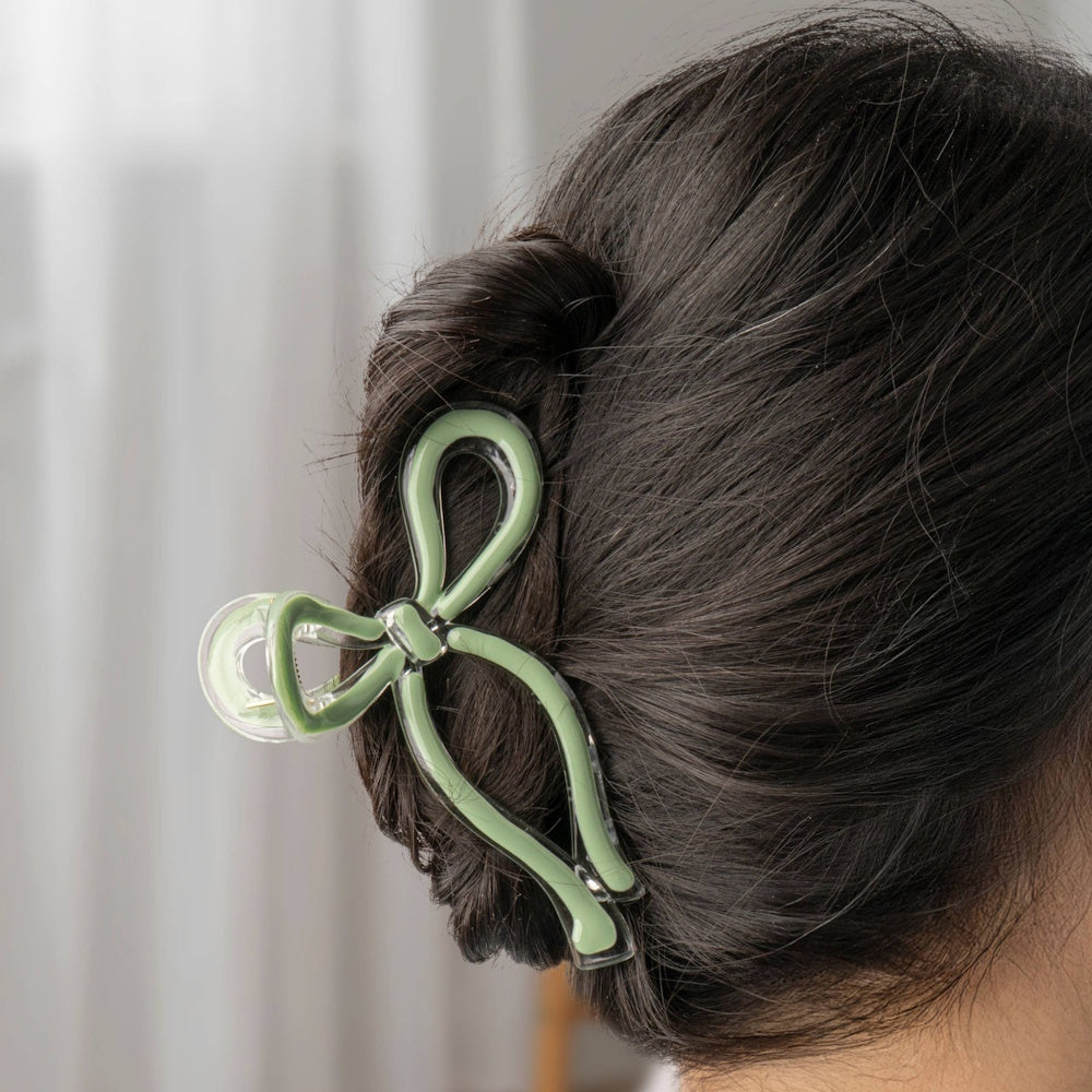 Clear green acrylic bow hair clip securing a dark hair bun in a simple, elegant style.