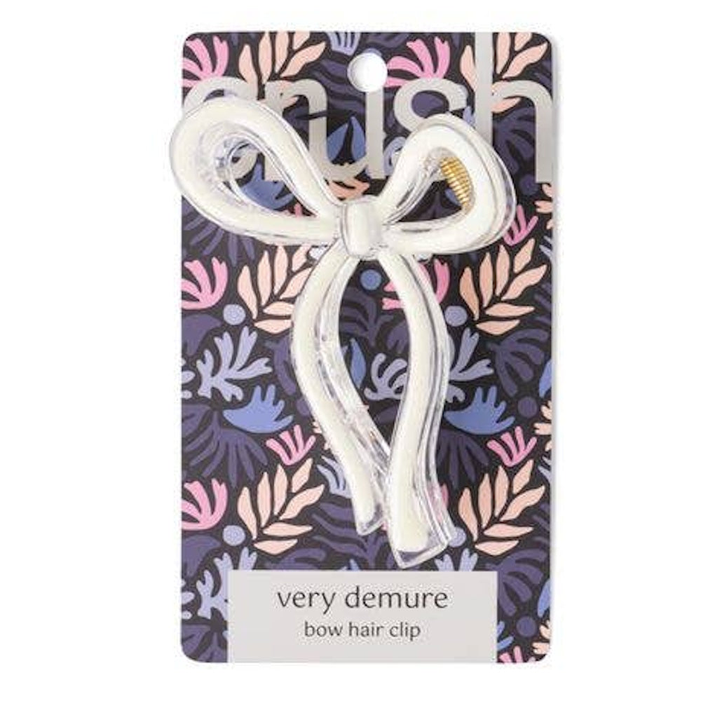 White very demure bow hair clip on a decorative floral background card. Simple, stylish accessory for hair styling.