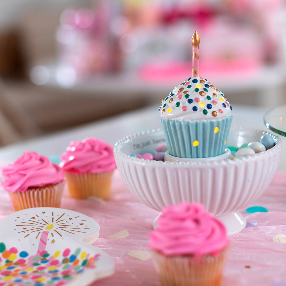 Ceramic light-up cupcake sitter with sprinkles and candle in a white fluted candy dish on a pink party table.