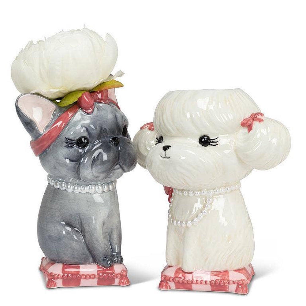 Two dog-shaped ceramic vases, a grey French bulldog and a white poodle, sitting on pink cushions.