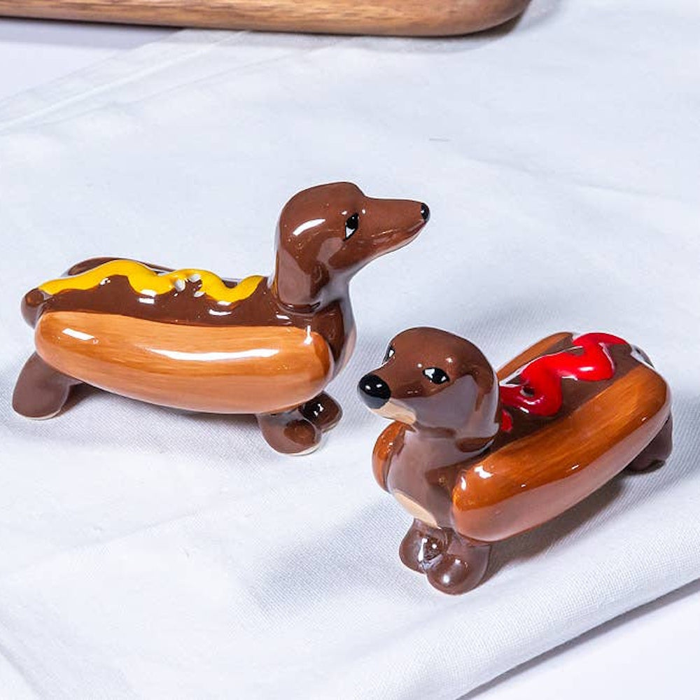 Ceramic salt and pepper shakers shaped like dachshund dogs inside hot dog buns with mustard and ketchup.