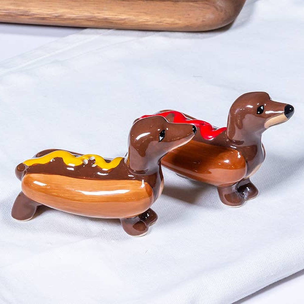 Ceramic salt and pepper shakers shaped like dachshund dogs tucked inside hot dog buns with condiments.