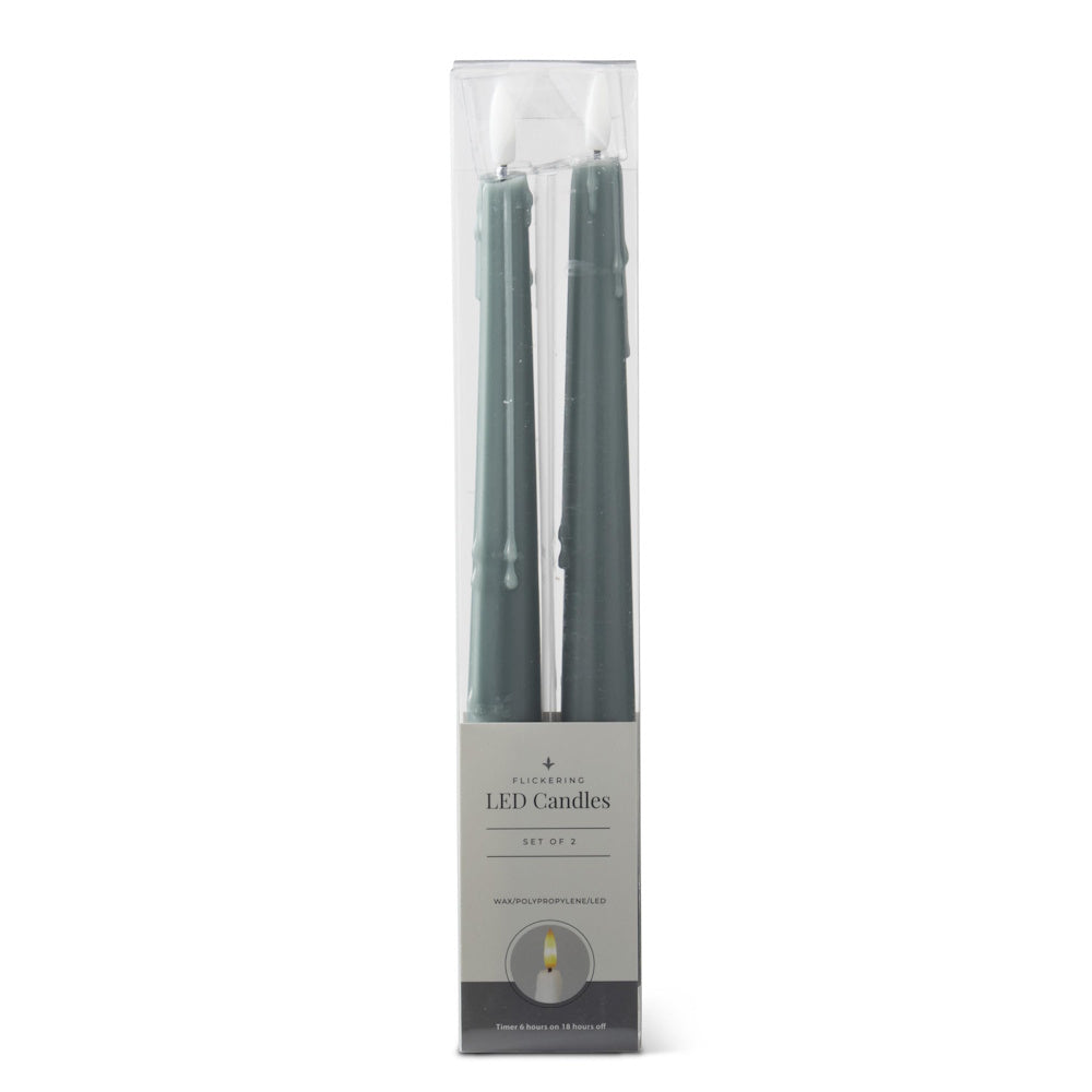 Set of 2 tall dark green flickering LED taper candles in a clear plastic packaging box against a white background.