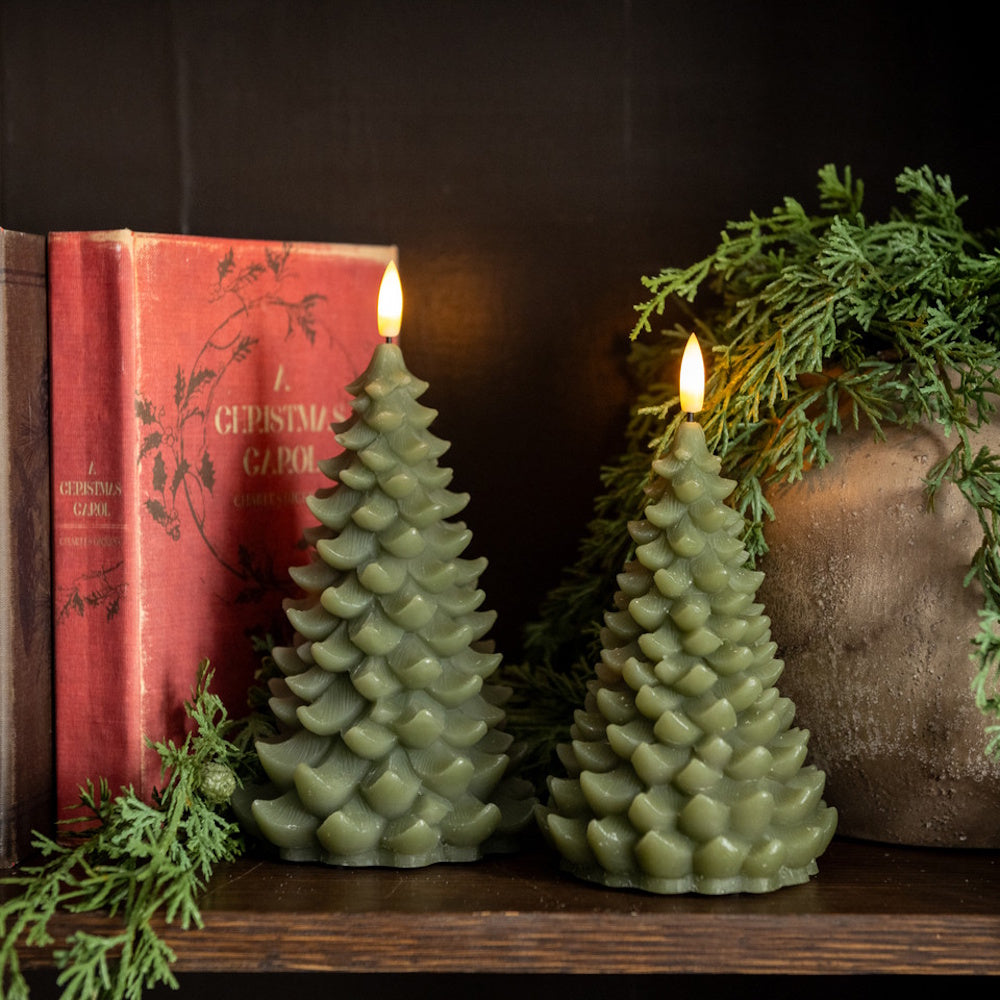Two green tree-shaped flameless candles glowing next to a red vintage book and evergreen greenery.
