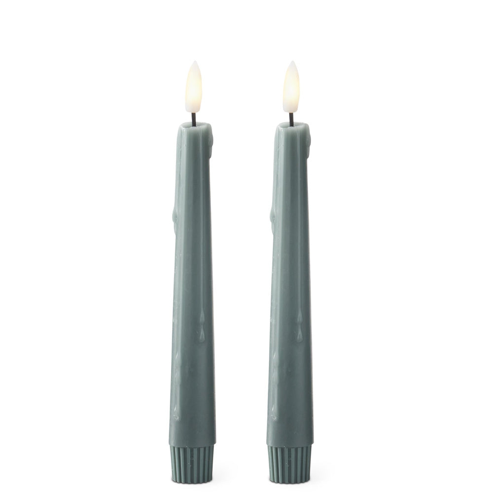 Pair of sage green drip-effect LED taper candles with glowing faux flames against a white background.
