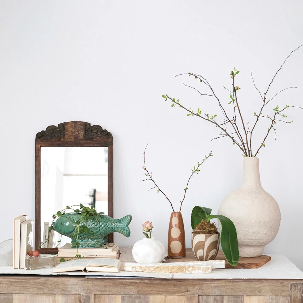 Green debossed fish planter and various ceramic vases with plants on a wooden console table against a white wall.